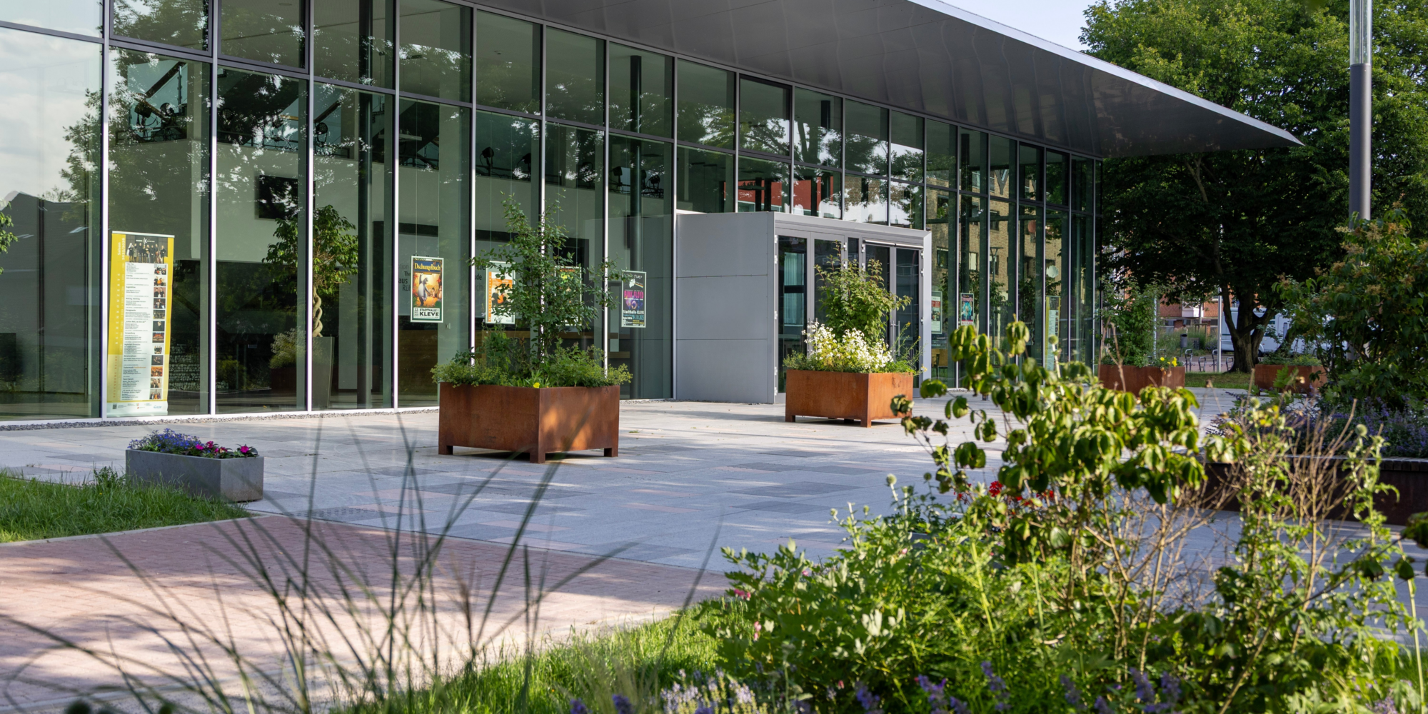 Bild von der Klever Stadthalle im Hintergrund, im Vordergrund Sträucher und Pflanzen
